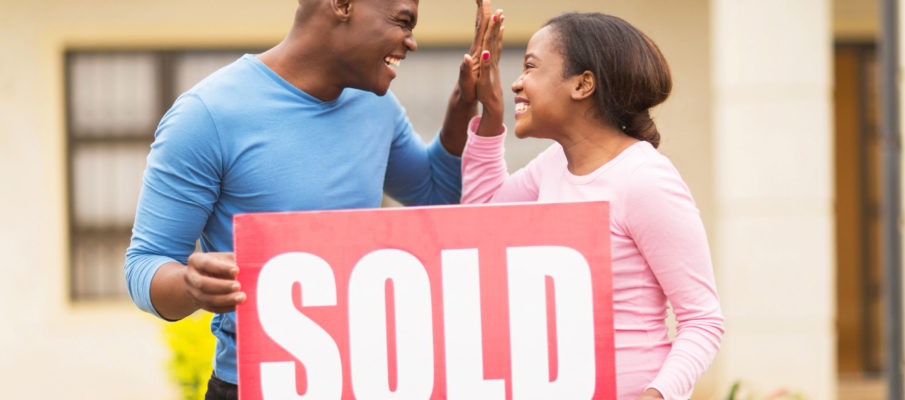 cheerful young black couple holding sold sign and celebrating their house been sold