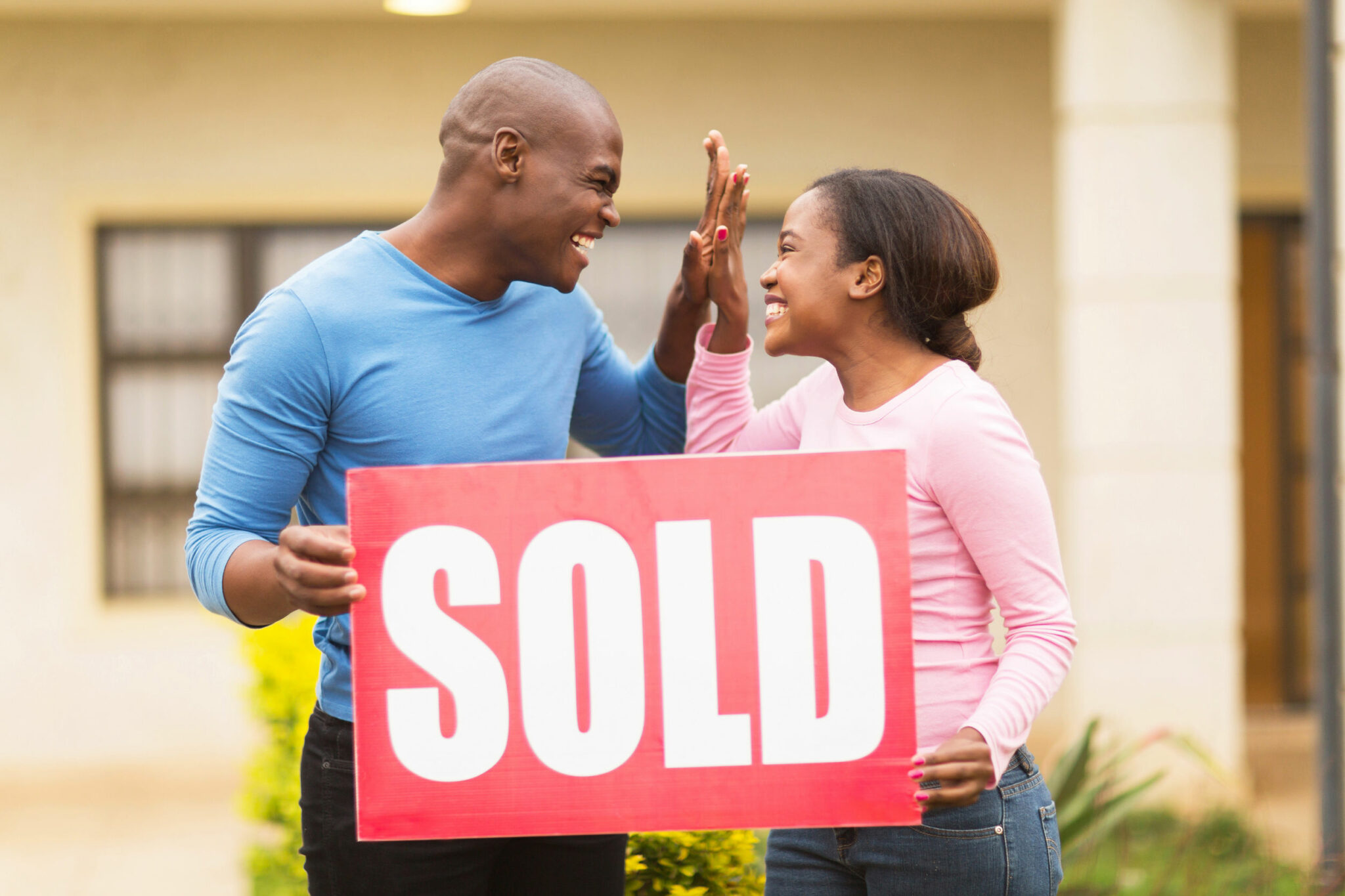 cheerful young black couple holding sold sign and celebrating their house been sold